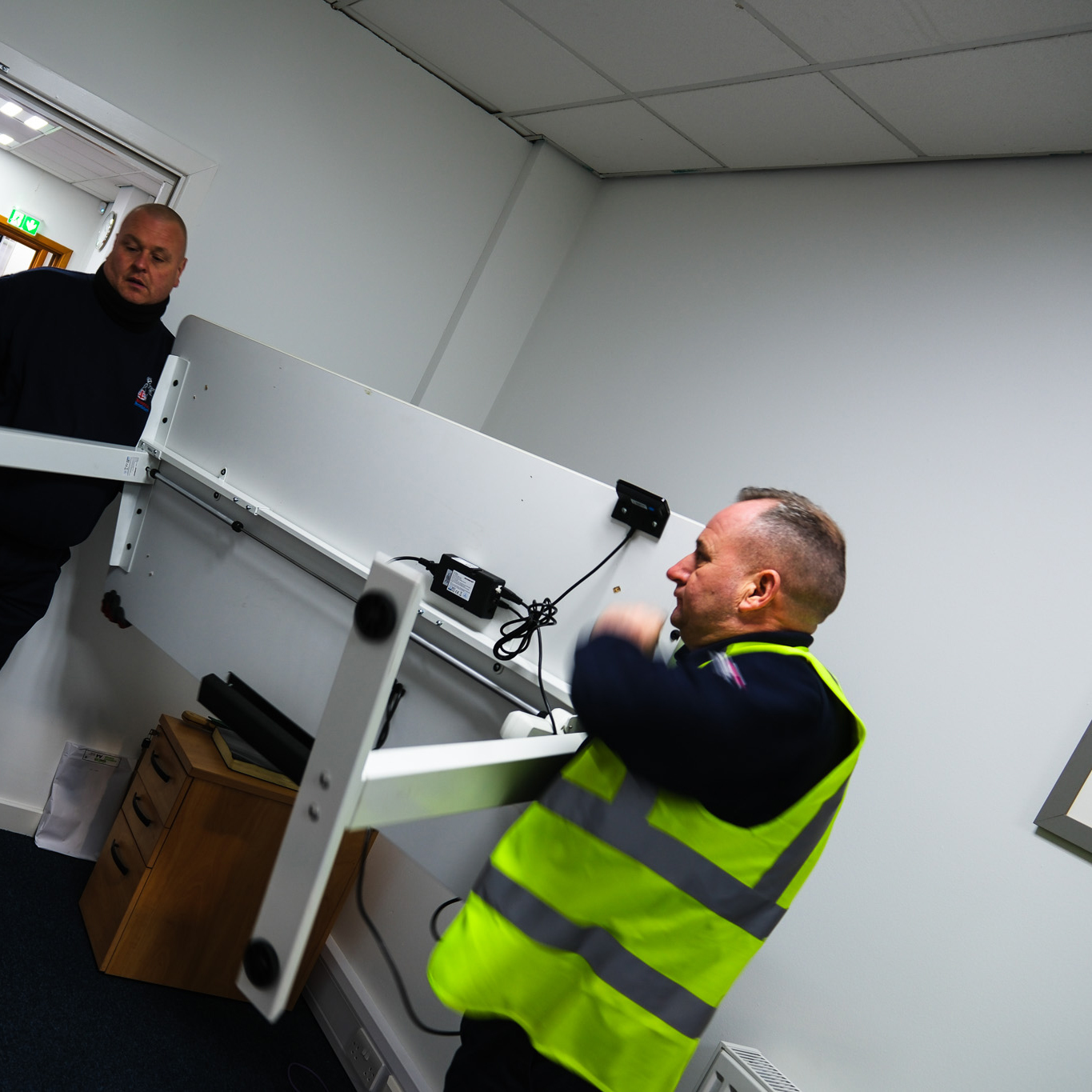 Two removal crew members carefully handling an office desk